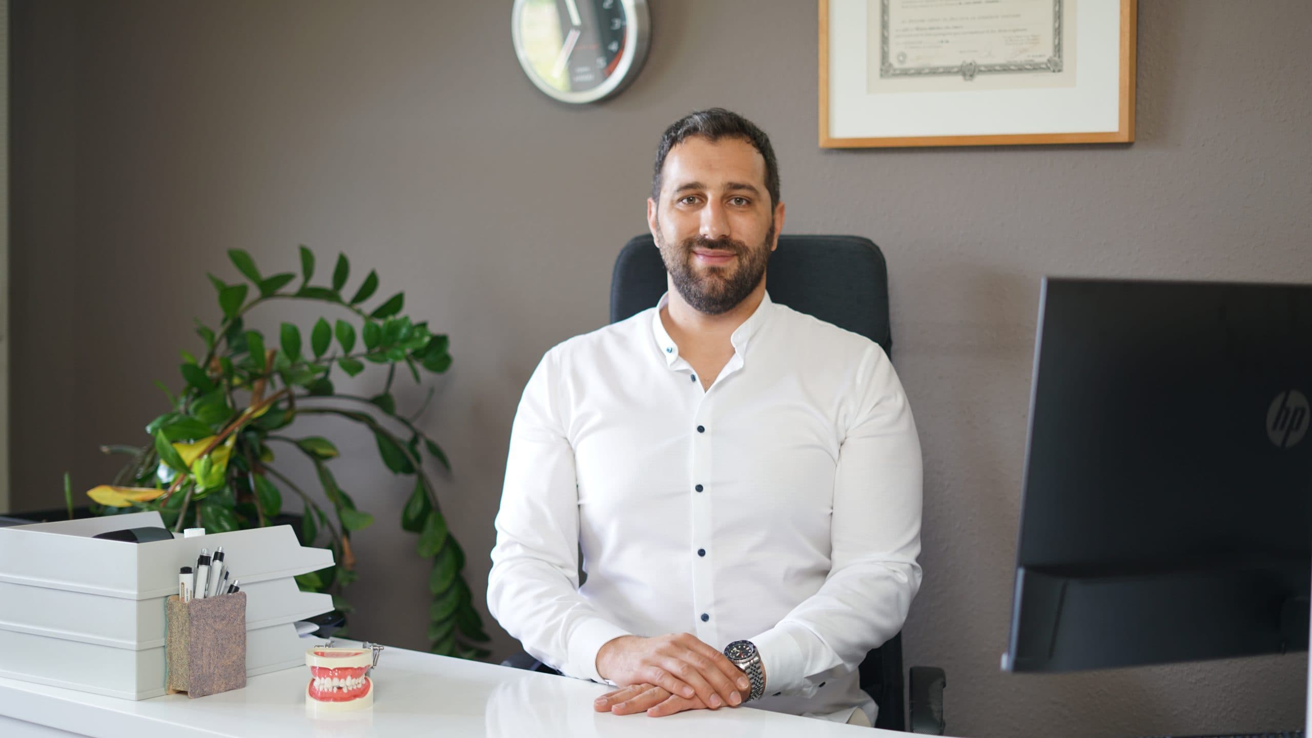 Le Dr. Amir Strukan à son bureau au cabinet, en chemise blanche, son diplôme encadré au mur derrière lui