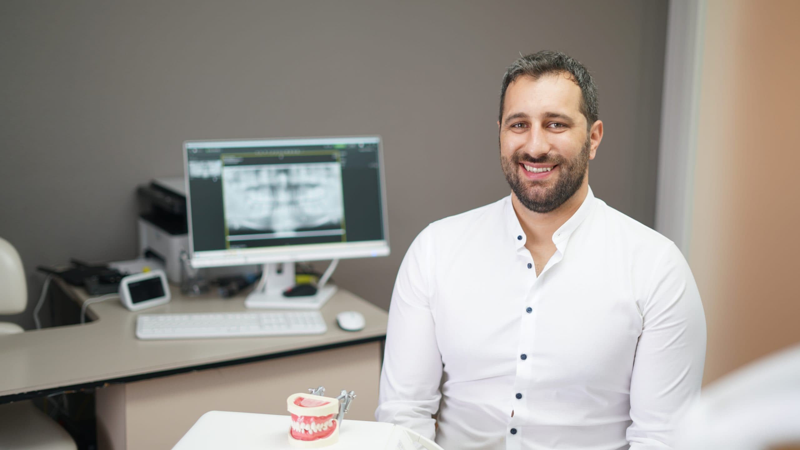 Le Dr. Amir Strukan à côté d’un écran affichant une radiographie panoramique, un modèle d’étude devant lui